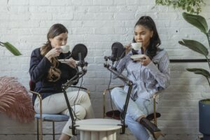 Two women enjoy coffee while recording a podcast indoors.