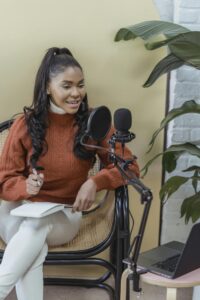 Young woman recording a podcast with a microphone and laptop in a cozy indoor setup.